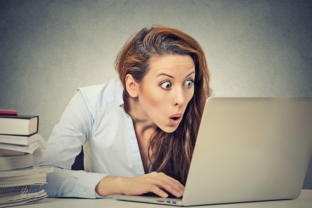 Portrait young shocked business woman sitting in front of laptop computer looking at screen isolated grey wall background. Funny face expression emotion feelings problem perception reaction Portrait young shocked business woman sitting in front of laptop computer looking at screen isolated grey wall background. Funny face expression emotion feelings problem perception reaction